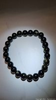 Obsidian bracelet laid flat in circular shape on light background showing round black beads with golden sheen flashes.