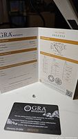 Photo showing moissanite gemstone, GRA certificate with grading results and gem proportions, and warranty card with ID number visible.