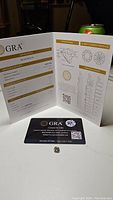 Photo of GRA grading report open showing details of the certified moissanite stone with the gemstone placed in front.