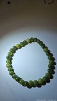 Green jade bracelet composed of polished round beads arranged in a circle, shown against a white background with shadows reflecting bead shapes.