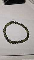 Photo of round forest green jade bead bracelet laid flat showing bead arrangement and color variation.