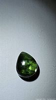 Pear-shaped natural green tourmaline cabochon gemstone with visible inclusions, shown against a plain background.