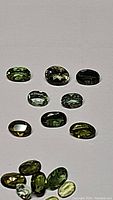 Top view of multiple oval cut green tourmaline gemstones laid out on a flat surface, showing size and color variation among 14 stones.