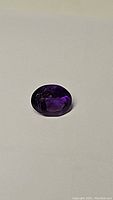 Oval cut deep purple amethyst gemstone on white background, showing faceted top view.