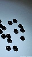 16 round jet black onyx cabochon gemstones arranged on a flat white surface showing their smooth polished finish and size.