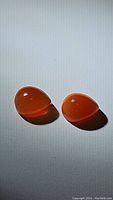 Pair of smooth pear-shaped Mandarin orange Carnelian cabochon gemstones glowing under torch light on white background