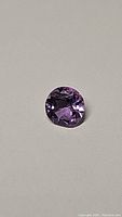 Close-up image of a round cut purple amethyst gemstone showing deep rich color and facet reflections.