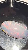 Close-up image of oval cabochon fire opal in ambient light showing red and orange flashes with luminous depth.