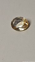 Close-up photo of the oval cut natural golden citrine gemstone on a white background, showing facets and light yellow color.