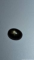 Oval cabochon black star sapphire gemstone showing star pattern clearly on surface under light.