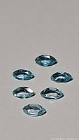 Six marquis cut Paraiba blue Apatite gemstones arranged on a flat surface.
