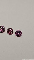 Photo showing three round cut pink garnet gemstones with bright and vivid pink color on a light surface.
