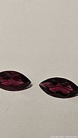 Pair of deep pink-purple Umbalite garnet gemstones on a neutral background, showing faceted marquise cut and clarity.