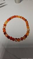 Natural red agate bead stretchy bracelet displayed on white background showing round beads with varied red and orange tones.