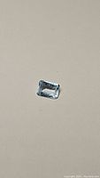 Close-up photo of a single loose sky blue topaz gemstone cut in an emerald rectangular shape, showing facets and light blue color on neutral background.