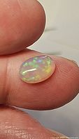Oval cabochon natural Ethiopian opal held on fingertip showing brilliant play of color with a galaxy-like pattern in blue and green hues.