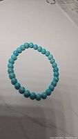 Photo showing turquoise bead stretchy bracelet laid flat on a light surface, round beads with natural turquoise coloration.
