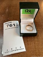 Ring displayed in green jewelry box with white interior, showing condition and size sticker on the box lid.