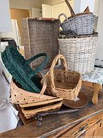 Photo showing an assortment of woven baskets in various sizes and colors stacked on and beside a wooden massager and part of a prayer bench.