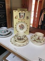 Dishes showing three Royal Doulton Bunnykins sets including boxed 3-piece set, plus two additional sets on a tabletop.