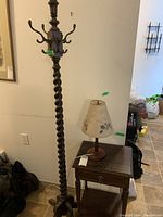 Full view of twisted wood coat rack with eight hooks alongside wood side table and lamp