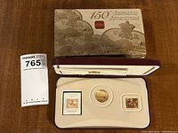 Overview of the commemorative coin, stamp, rectangular gold-plated piece, and their display box with anniversary information on lid.