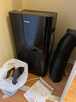 Black Danby portable air conditioner unit, flexible exhaust hose, remote control, and spare parts bag visible near unit