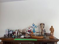 Wide view of assorted decorative items on table including wooden model ship, folk art carvings, stained glass, antique salt and pepper shakers, cloisonné pieces, and other small decorative figurines.