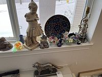 Wide shot of the windowsill showing all decorative items in the lot including figurines, paperweights, vases, and the decorative plate.