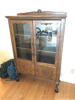 Front view of the wooden display cabinet showing glass doors, bottom doors, and carved crest