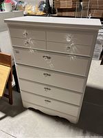 Front view of white painted highboy dresser showing two small top drawers with clear glass knobs and four larger drawers beneath with decorative metal handles.