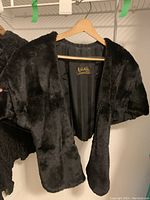 Full view of the black mink fur shawl hanging on a wooden hanger showing the fur texture and shape.