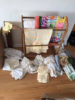 Wooden quilt rack with multicolor crocheted afghan quilts and assorted folded linens on the floor
