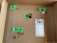 Multiple men's jewelry items arranged in a cardboard box labeled with gold karat markings (6F, 10K, 12K GF) and an auction lot card