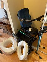 Overview photo showing the Evolution walker with its blue padded seat, the Everlasting Comfort seat cushion, and two white plastic toilet assist seats placed on the floor nearby.