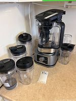 Full view of the Ninja blender base with large pitcher and four additional blending cups with lids on a counter.