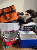 Photo of lot showing Playmate Elite cooler, colorful insulated picnic bag, boxed air mattress, folded throws and boxed duvet.