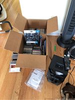 Photo showing cardboard box filled with CDs and packaged HDMI cable, Sony stereo unit nearby on floor, user manual in plastic bag.