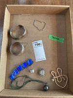 Top-down view of all items arranged in box showing bracelets, necklaces, rings, glass panel bracelet and bell