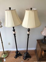 Pair of standing floor lamps with cream fabric bell shades and dark ornate bases with beige stone spheres.