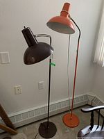 Pair of vintage metal floor lamps, one dark brown and one orange, standing side by side showing full height and design.