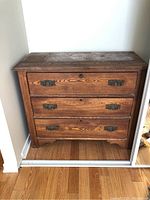 Full view of the front of the wooden dresser showing the three drawers, metal handles, and wood grain.