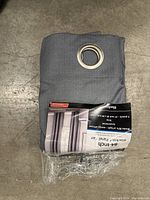 Folded gray blackout curtain panel with silver metal grommet at top, partially wrapped in plastic.
