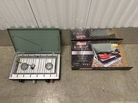 Photo of Coleman Cascade propane camping stove open with two burners showing and original box next to it