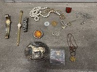 Full display of costume jewelry items laid out on a surface including watches, bracelets, necklaces, pins, and belt buckle.