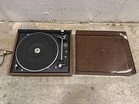 Full view of the Dual turntable next to its clear dust cover with damaged corner.