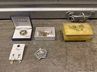 Overview of the lot showing the Crescent necklace in box, a white box with assorted jewelry pieces, Majestique clip-on earrings on card, rhinestone brooch, and yellow floral jewelry box