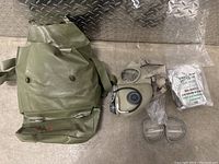 Overall lot showing gas mask, attached eyepieces, carrying bag, sealed filter, and extra eyepieces in plastic wrapping.