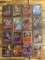 Full view of 16 Pokemon V cards arranged in 4x4 grid on a wooden surface, each in clear protective sleeve.