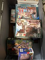 Overview of assorted jigsaw puzzle boxes including Ravensburger and dog-themed puzzles, stacked in container